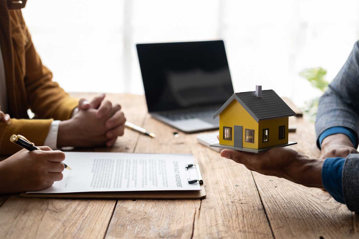 Law Firm's attorneys in a discussion, with a focus on a red-roofed house model on the table, indicating real estate law services.