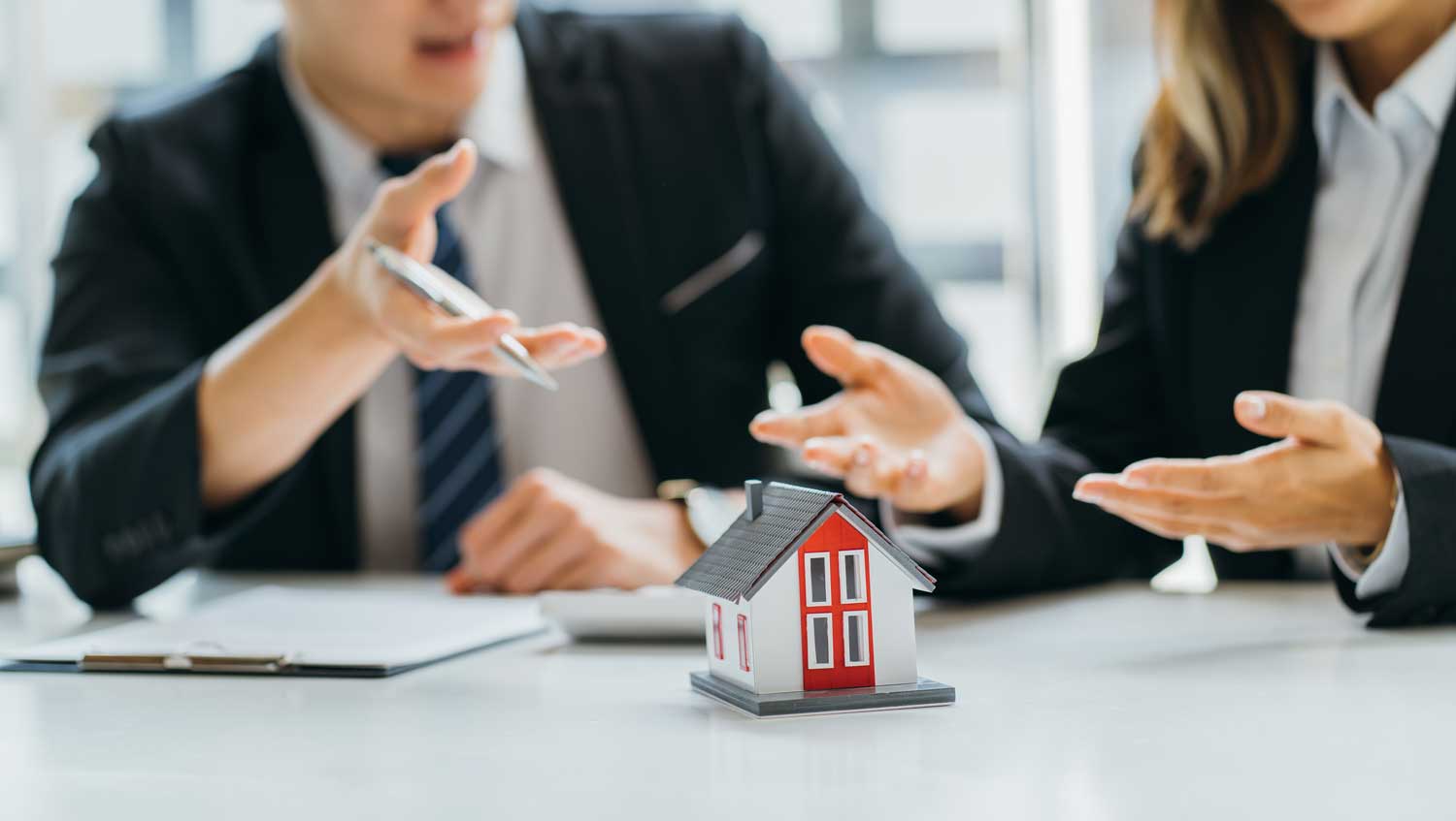 A Law Firm's attorneys in a discussion, with a focus on a red-roofed house model on the table, indicating real estate law services.