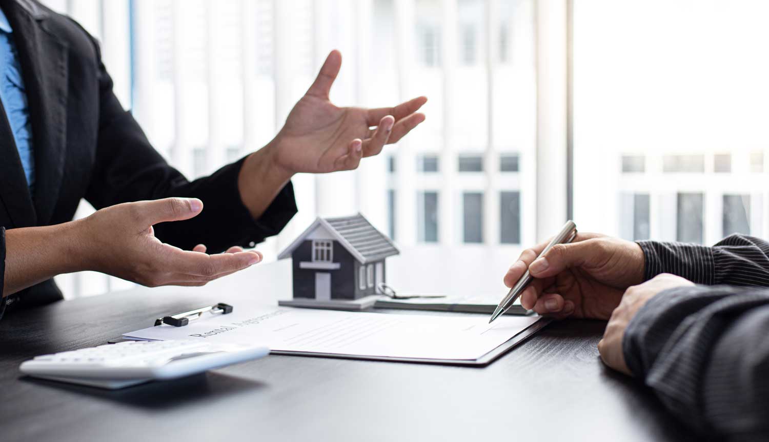 Law Firm legal consultation in progress with a client signing paperwork, a model home on the desk.