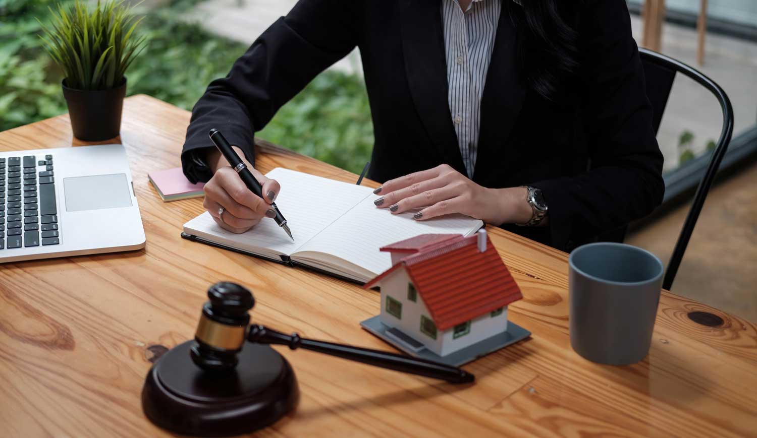 SKB Law Firm attorney drafting legal documents, with a laptop, gavel, and model home on the office desk.