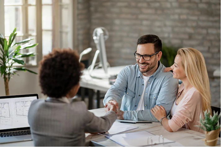 Two satisfied clients shaking hands with a professional at SKB Law Firm, expressing contentment with legal services provided, in a modern office setting with architectural plans on display.